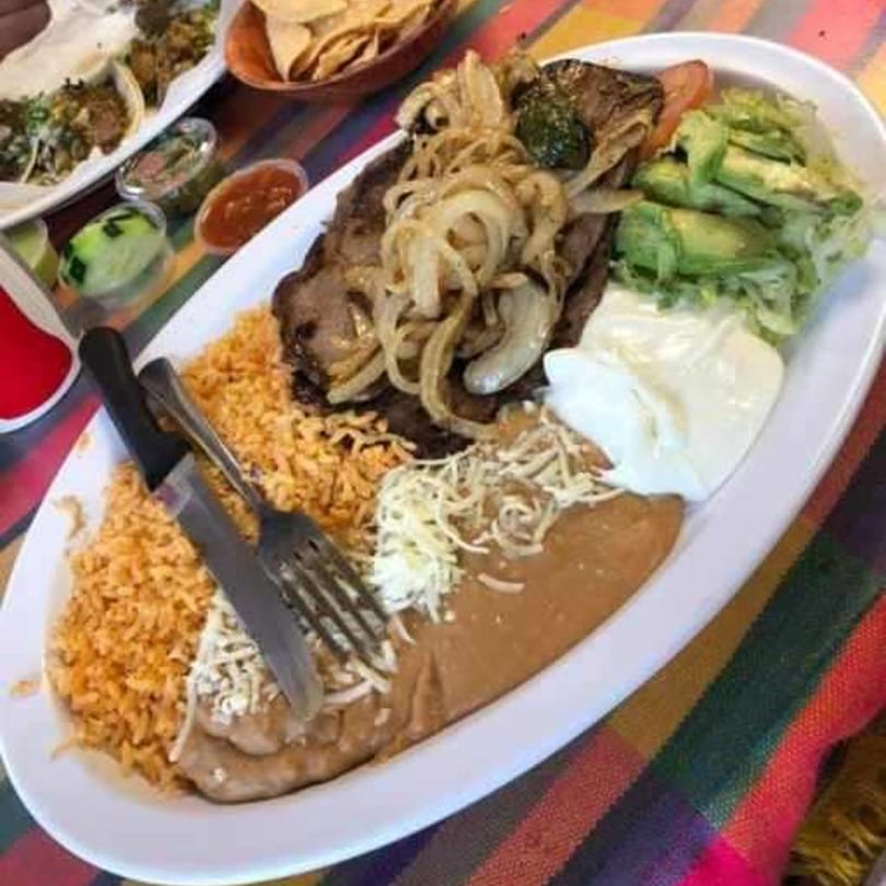 Mexican steak fajita with rice, beans, avocado, sour cream, and grilled onions on a white platter.